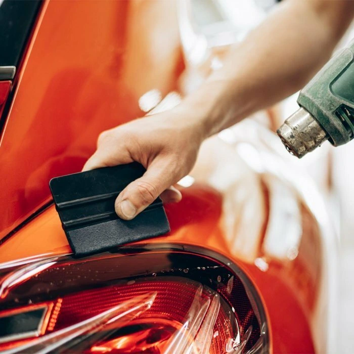 Applying paint protection film (PPF) on a red car with a heat gun and scraper tool in Abu Dhabi for premium car protection.